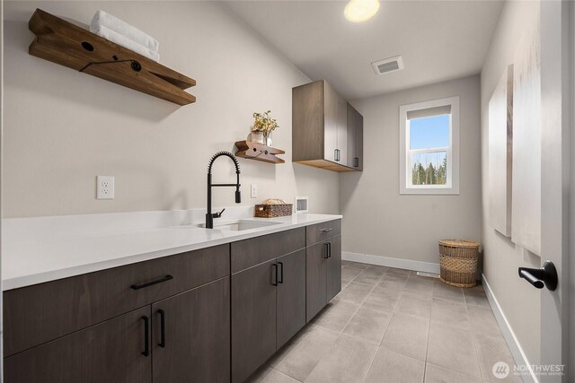 laundry area featuring cabinet space, baseboards, visible vents, a sink, and light tile patterned flooring