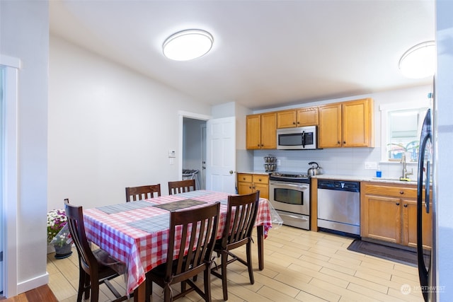 kitchen featuring appliances with stainless steel finishes, sink, light hardwood / wood-style flooring, and backsplash