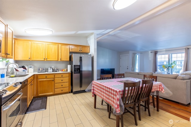 kitchen featuring sink, vaulted ceiling with beams, light hardwood / wood-style flooring, stainless steel appliances, and decorative backsplash