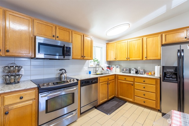 kitchen featuring sink, vaulted ceiling, appliances with stainless steel finishes, light stone countertops, and decorative backsplash