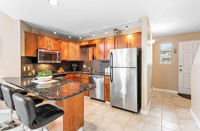 kitchen featuring kitchen peninsula, stainless steel appliances, backsplash, dark stone countertops, and a kitchen breakfast bar