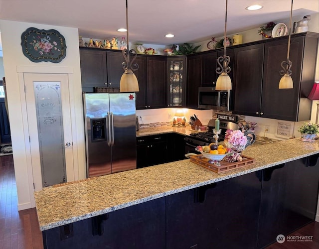 kitchen with dark brown cabinetry, stainless steel appliances, decorative light fixtures, and kitchen peninsula