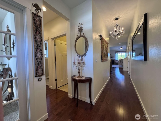 hallway featuring baseboards, a chandelier, and hardwood / wood-style flooring