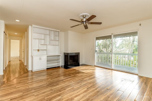 unfurnished living room featuring a multi sided fireplace, ceiling fan, and light wood-type flooring