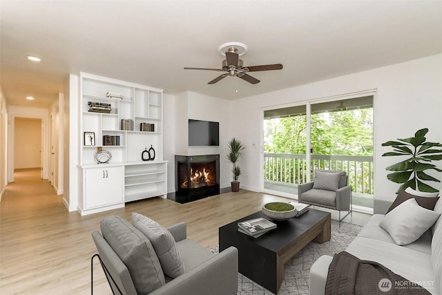 living room with baseboards, a fireplace with flush hearth, ceiling fan, and light wood-type flooring