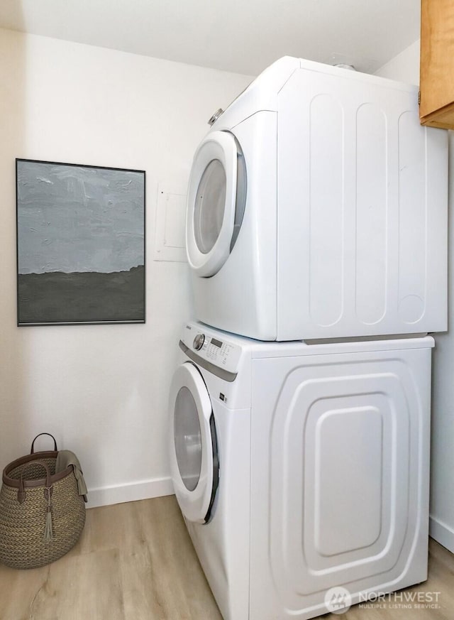 clothes washing area with laundry area, stacked washer and dryer, light wood finished floors, and baseboards