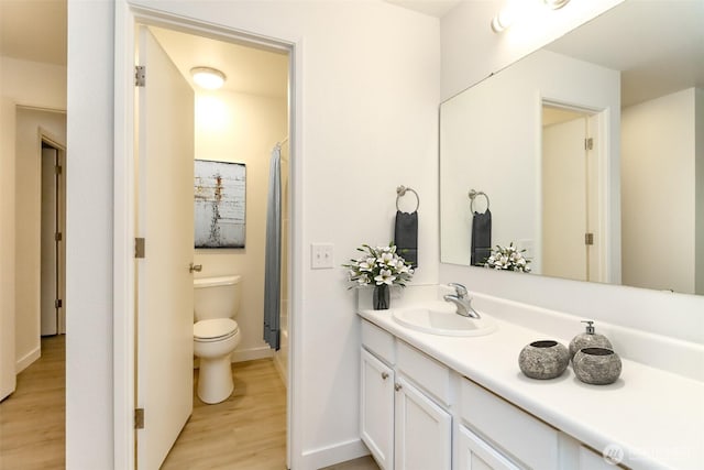 full bath featuring a shower with curtain, wood finished floors, baseboards, vanity, and toilet