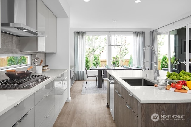 kitchen with wall chimney range hood, plenty of natural light, sink, and stainless steel gas stovetop