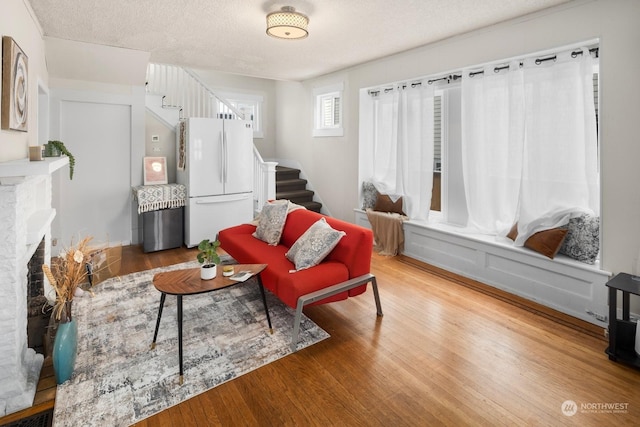 living area with a brick fireplace, hardwood / wood-style flooring, and a textured ceiling