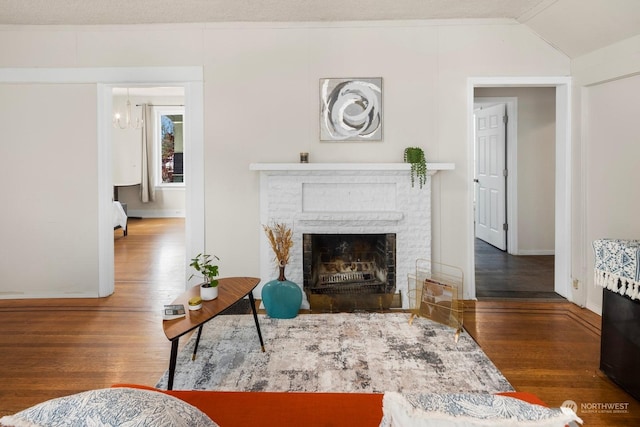 living room featuring lofted ceiling, dark hardwood / wood-style flooring, and a brick fireplace