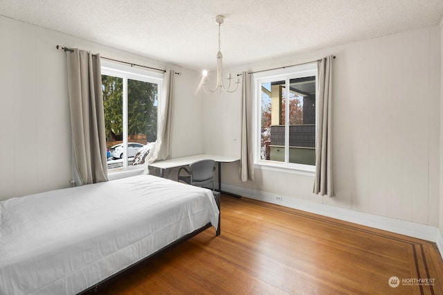 bedroom with a notable chandelier, wood-type flooring, multiple windows, and a textured ceiling