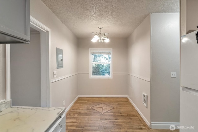 unfurnished dining area with light wood-type flooring, electric panel, visible vents, a notable chandelier, and a textured ceiling