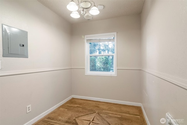 unfurnished room with a notable chandelier, electric panel, baseboards, a textured ceiling, and wood finished floors