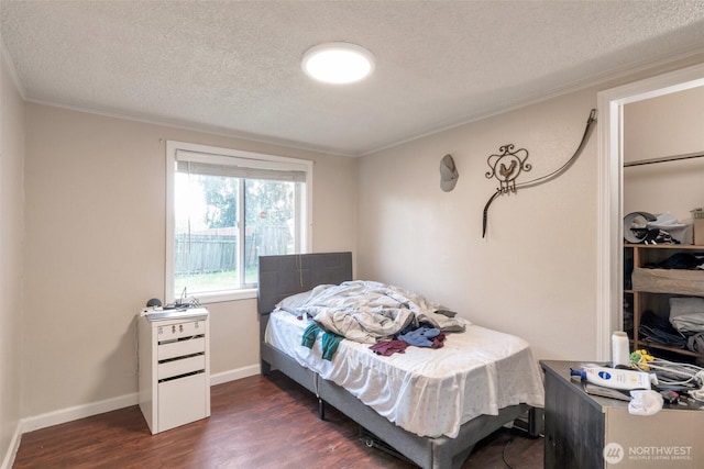 bedroom with a textured ceiling, crown molding, dark wood finished floors, and baseboards