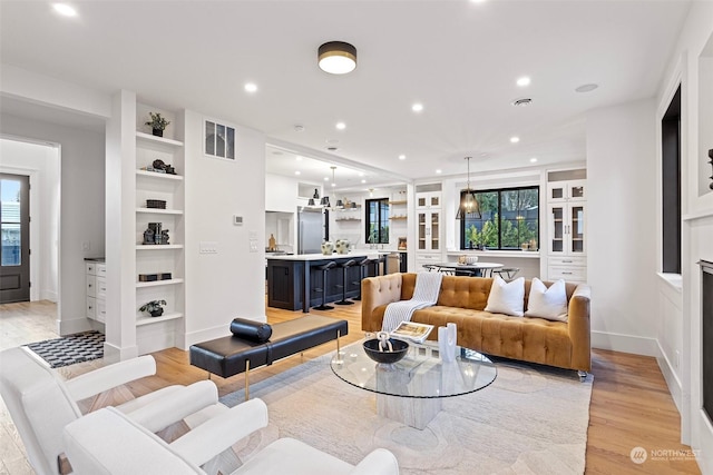 living room with built in shelves, a wealth of natural light, and light wood-type flooring