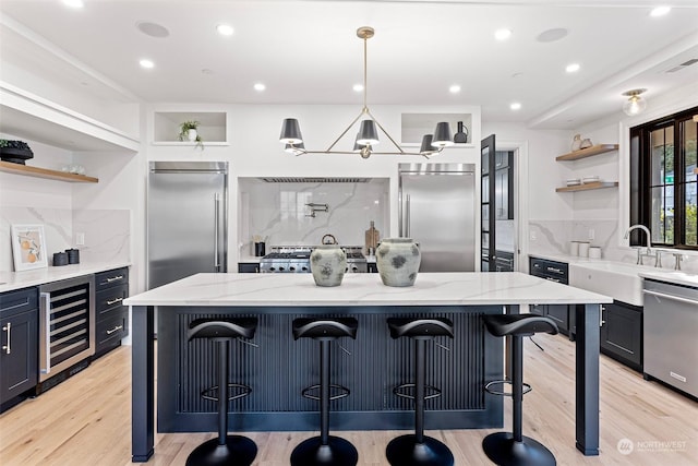 kitchen with a kitchen bar, a center island, appliances with stainless steel finishes, beverage cooler, and light stone countertops