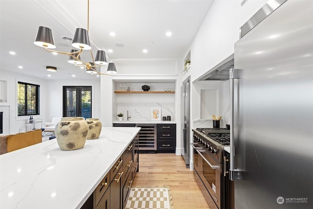 kitchen featuring pendant lighting, high quality appliances, light stone counters, light hardwood / wood-style floors, and beverage cooler