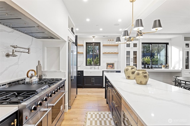 kitchen featuring sink, light stone counters, premium appliances, ventilation hood, and decorative light fixtures