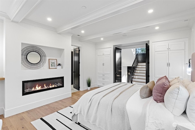 bedroom with crown molding, beam ceiling, and light hardwood / wood-style flooring