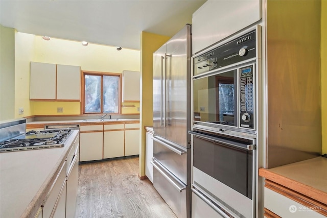 kitchen featuring appliances with stainless steel finishes, sink, white cabinets, and light hardwood / wood-style flooring