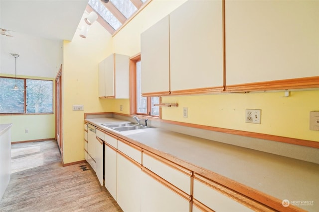 kitchen featuring sink, white cabinetry, a skylight, hanging light fixtures, and light hardwood / wood-style floors