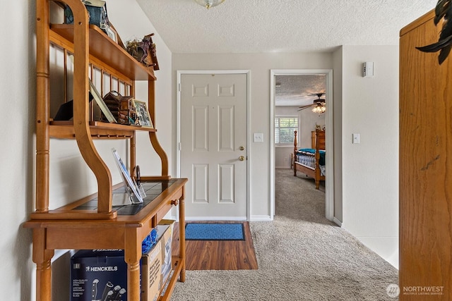 carpeted foyer entrance featuring baseboards, a ceiling fan, and a textured ceiling