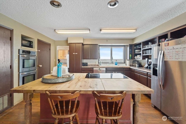 kitchen featuring stainless steel appliances, a center island, a textured ceiling, a kitchen bar, and dark hardwood / wood-style flooring