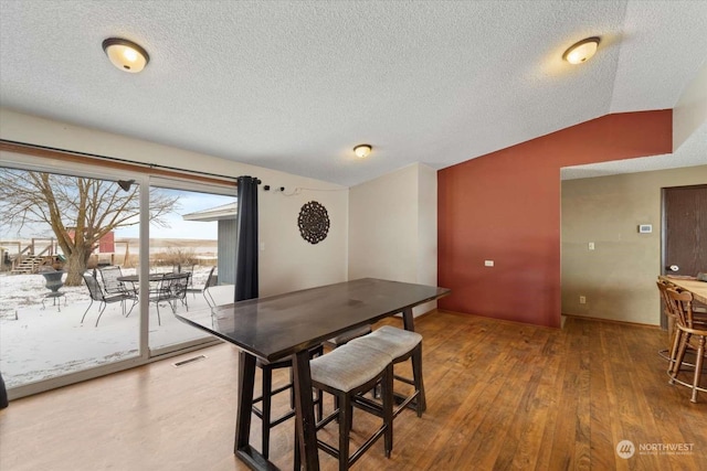 dining room with vaulted ceiling, hardwood / wood-style floors, and a textured ceiling