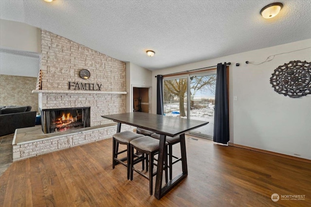 dining space featuring hardwood / wood-style flooring, vaulted ceiling, a textured ceiling, and a fireplace