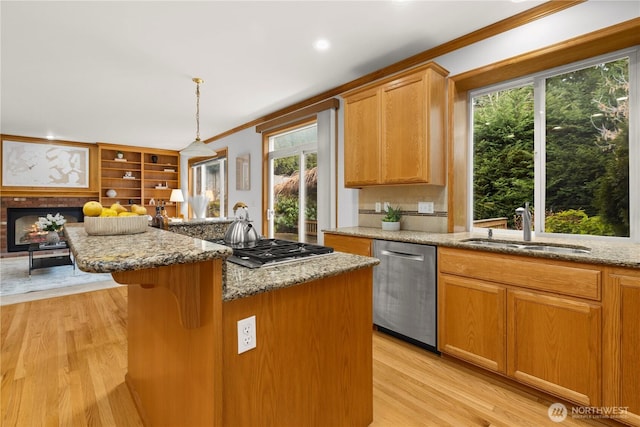 kitchen with appliances with stainless steel finishes, hanging light fixtures, a sink, light stone counters, and a kitchen island