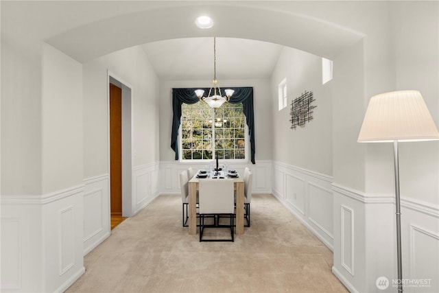 dining area featuring arched walkways, wainscoting, light carpet, and an inviting chandelier