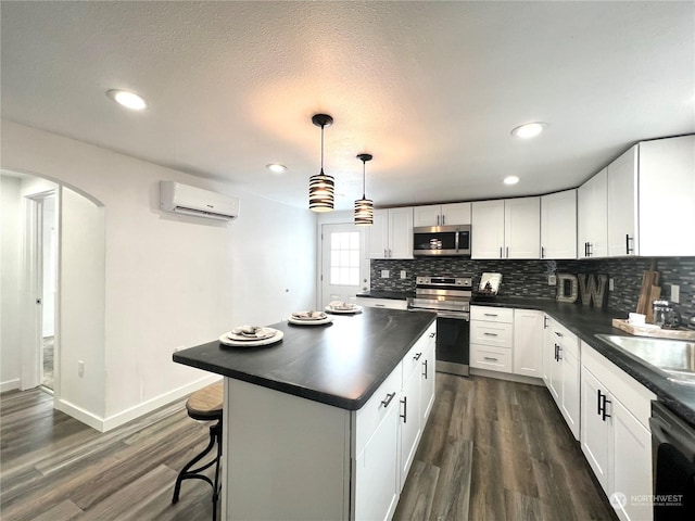 kitchen with sink, decorative light fixtures, an AC wall unit, appliances with stainless steel finishes, and white cabinets