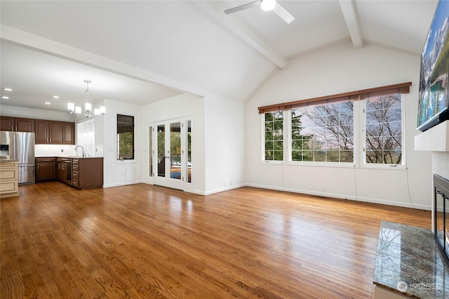 unfurnished living room featuring lofted ceiling with beams, sink, ceiling fan with notable chandelier, and light hardwood / wood-style flooring