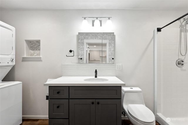 bathroom featuring stacked washing maching and dryer, backsplash, a tile shower, vanity, and toilet