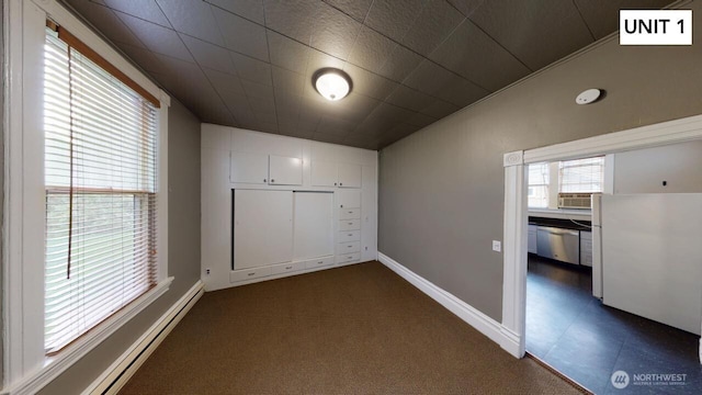 unfurnished bedroom featuring a baseboard heating unit, lofted ceiling, and dark colored carpet