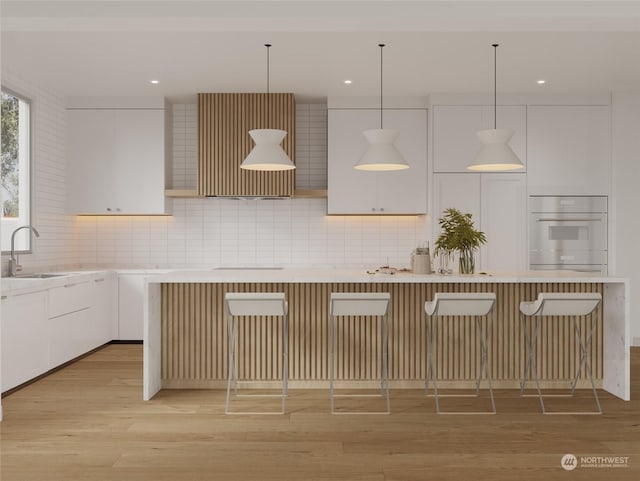 kitchen with a sink, a kitchen breakfast bar, light wood-style floors, white oven, and backsplash