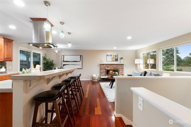 kitchen with a breakfast bar, pendant lighting, a fireplace, dark hardwood / wood-style flooring, and island exhaust hood