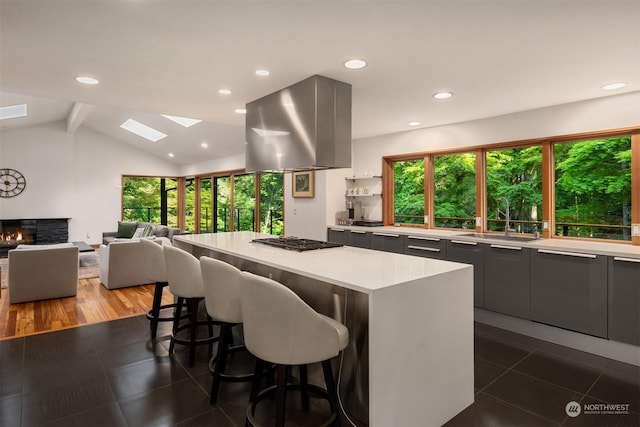 kitchen with sink, vaulted ceiling with skylight, island range hood, stainless steel gas cooktop, and a kitchen island