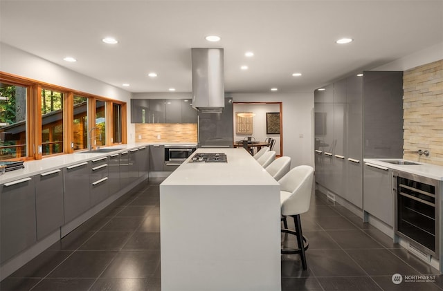 kitchen featuring wine cooler, a kitchen bar, gray cabinets, dark tile patterned flooring, and island exhaust hood