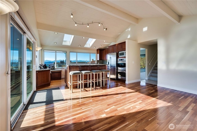 kitchen featuring dark hardwood / wood-style floors, a kitchen breakfast bar, a kitchen island, stainless steel appliances, and vaulted ceiling with skylight