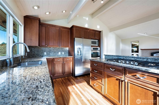 kitchen featuring lofted ceiling with beams, appliances with stainless steel finishes, sink, and light stone counters