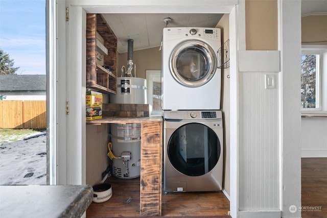 washroom featuring strapped water heater, stacked washing maching and dryer, dark wood finished floors, and laundry area