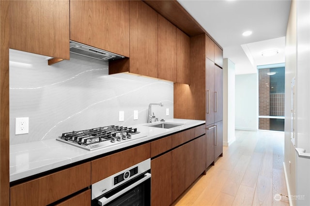 kitchen with sink, light hardwood / wood-style flooring, appliances with stainless steel finishes, range hood, and light stone countertops