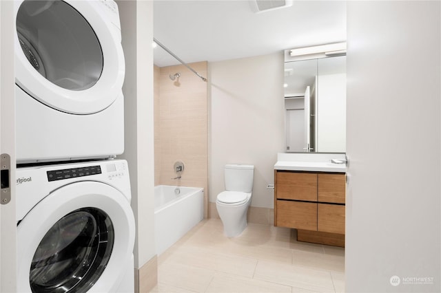 full bathroom with tiled shower / bath combo, vanity, stacked washer and clothes dryer, tile patterned flooring, and toilet