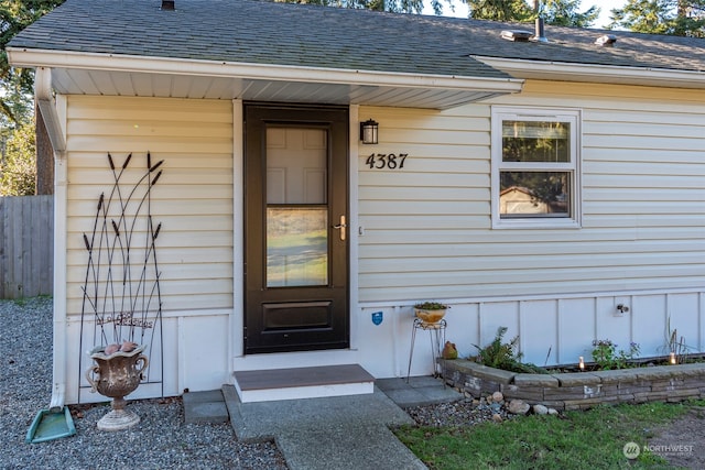 property entrance with roof with shingles and fence