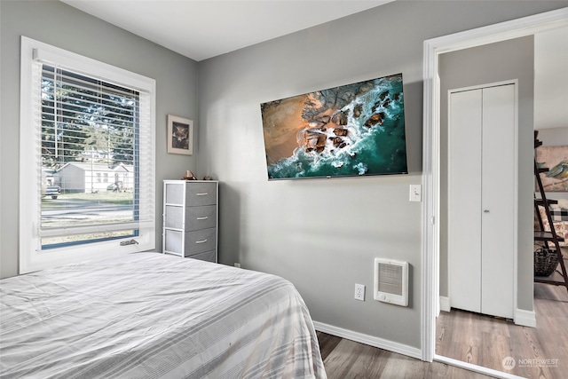 bedroom with baseboards, wood finished floors, and heating unit