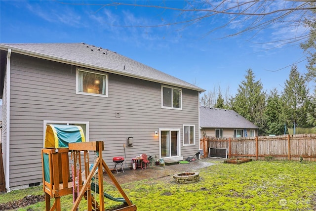 back of house with a fire pit, a lawn, and a playground