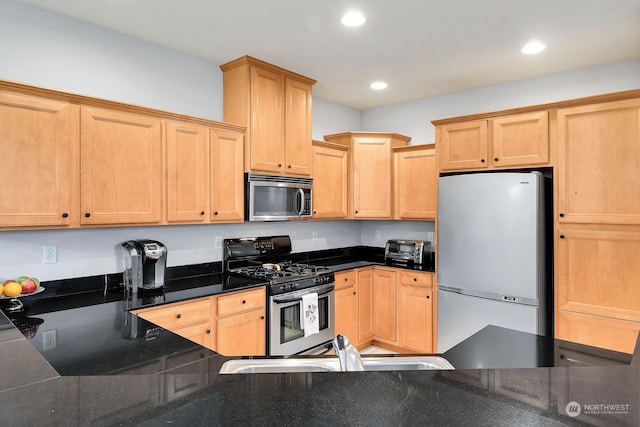 kitchen with stainless steel appliances, light brown cabinetry, sink, and dark stone counters