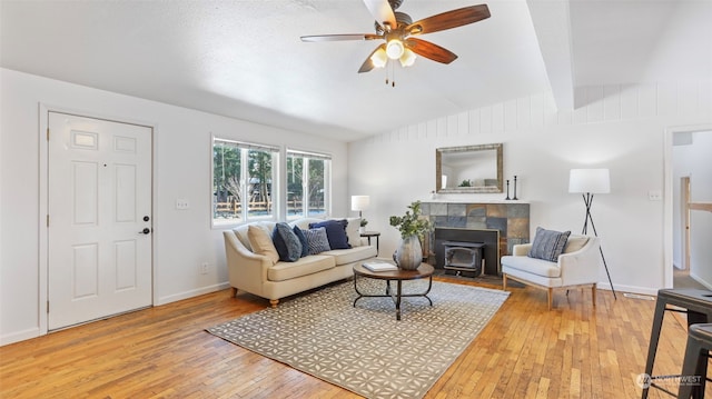 living room featuring vaulted ceiling with beams, hardwood / wood-style floors, ceiling fan, and a wood stove