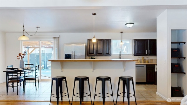 kitchen featuring a breakfast bar, stainless steel appliances, dark brown cabinetry, a kitchen island, and decorative light fixtures